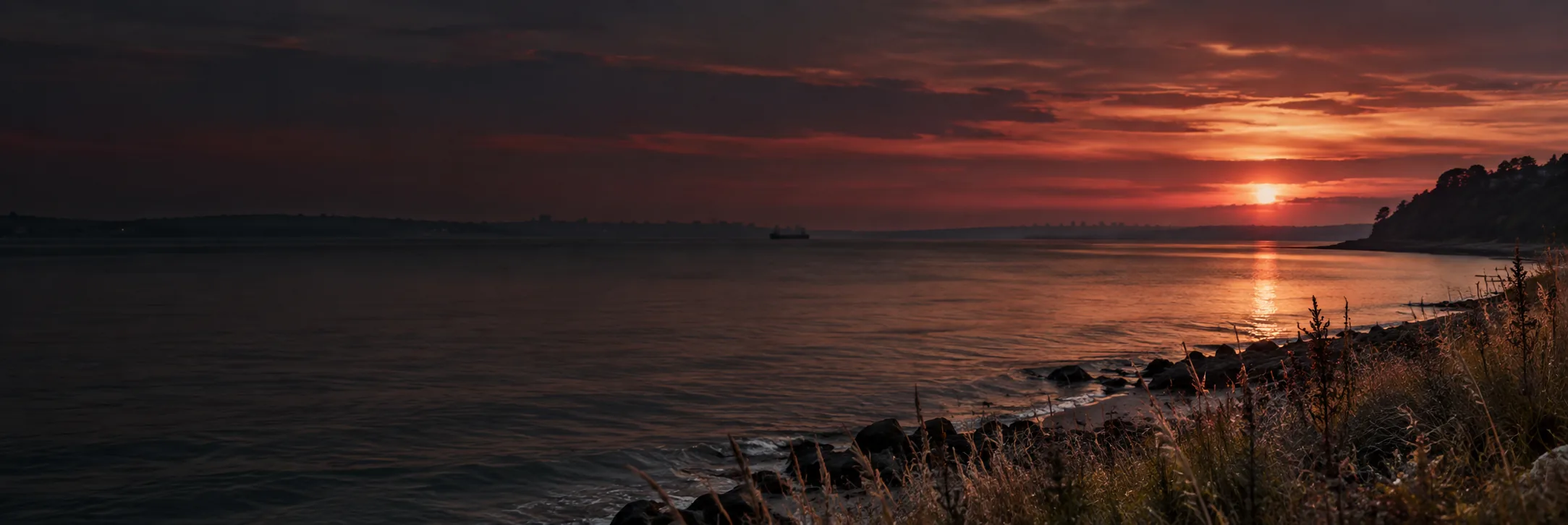 Rocky shoreline at dusk with the sun setting over calm water